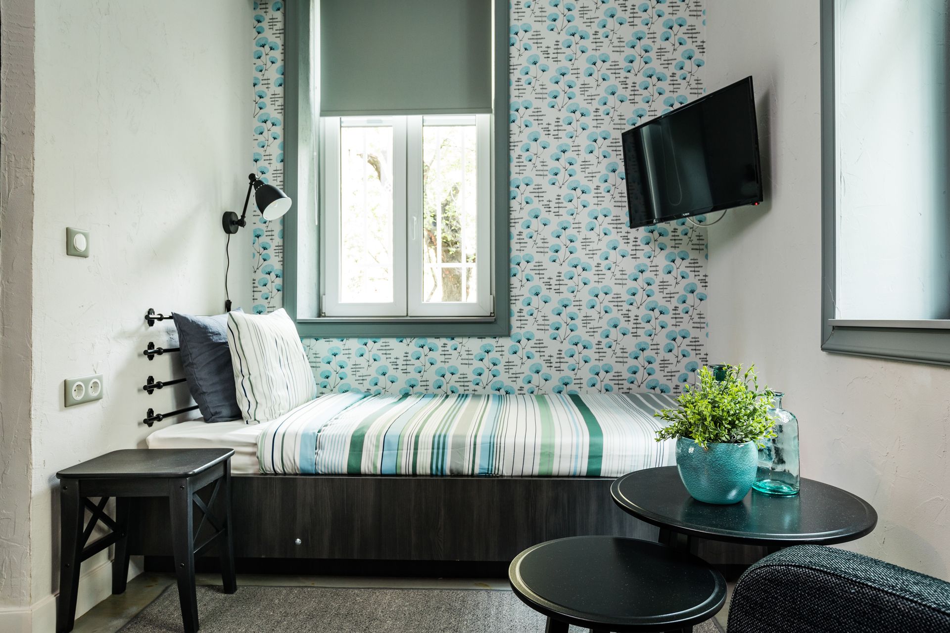 A compact room with a bed, a small table, a wall-mounted TV, and a window with a view.