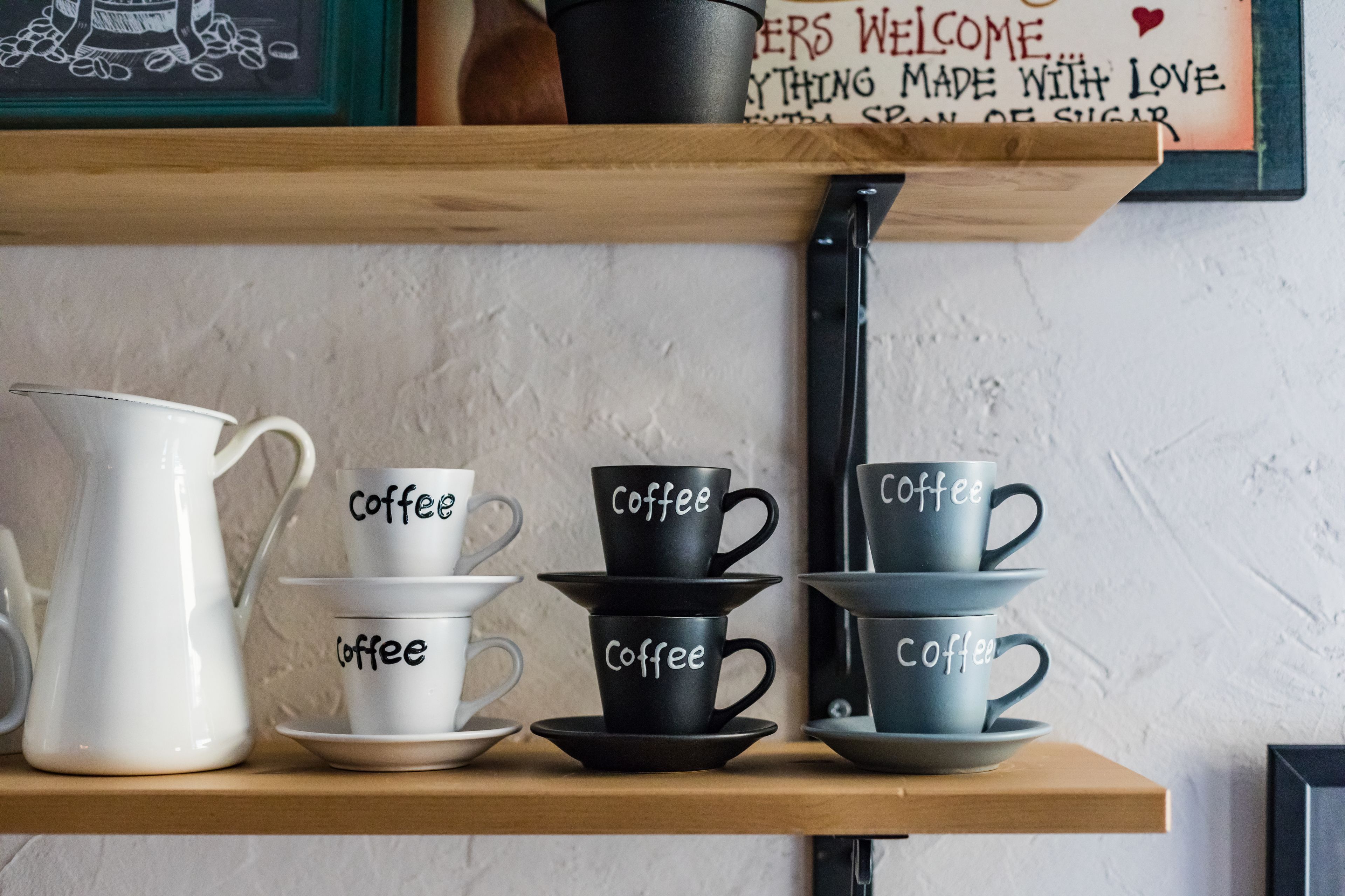 Una repisa con tazas de café y una jarra, dispuestas sobre un estante de madera frente a una pared texturizada.