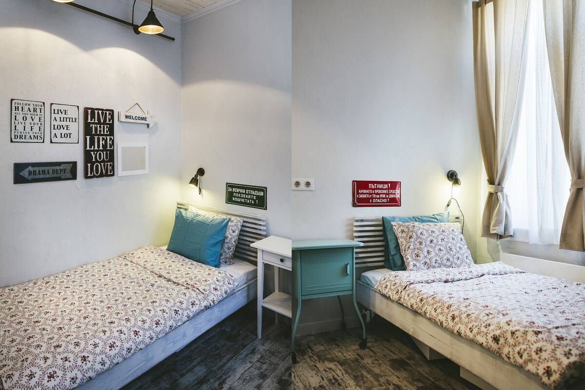 A dormitory room with two single beds, a small desk, and a wall with motivational signs.