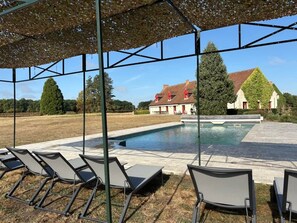 Zona de piscina amb gandules, un espai d'estar cobert i vista cap a cases al fons.