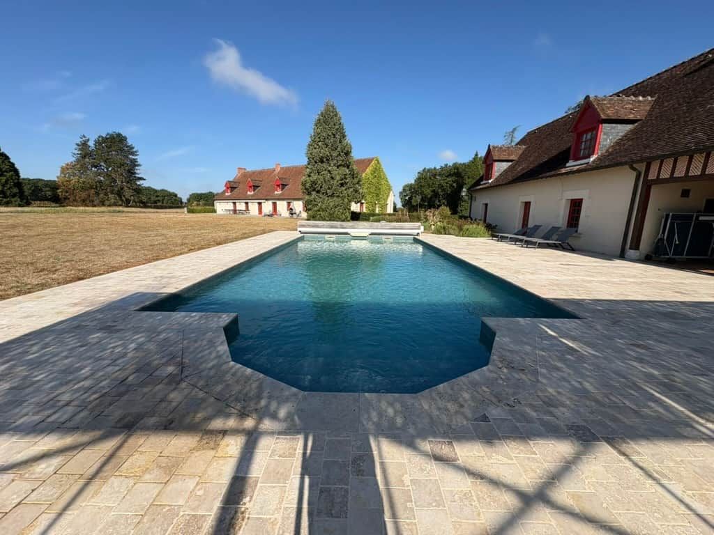 Una piscina con diseño geométrico, rodeada de un solárium empedrado.