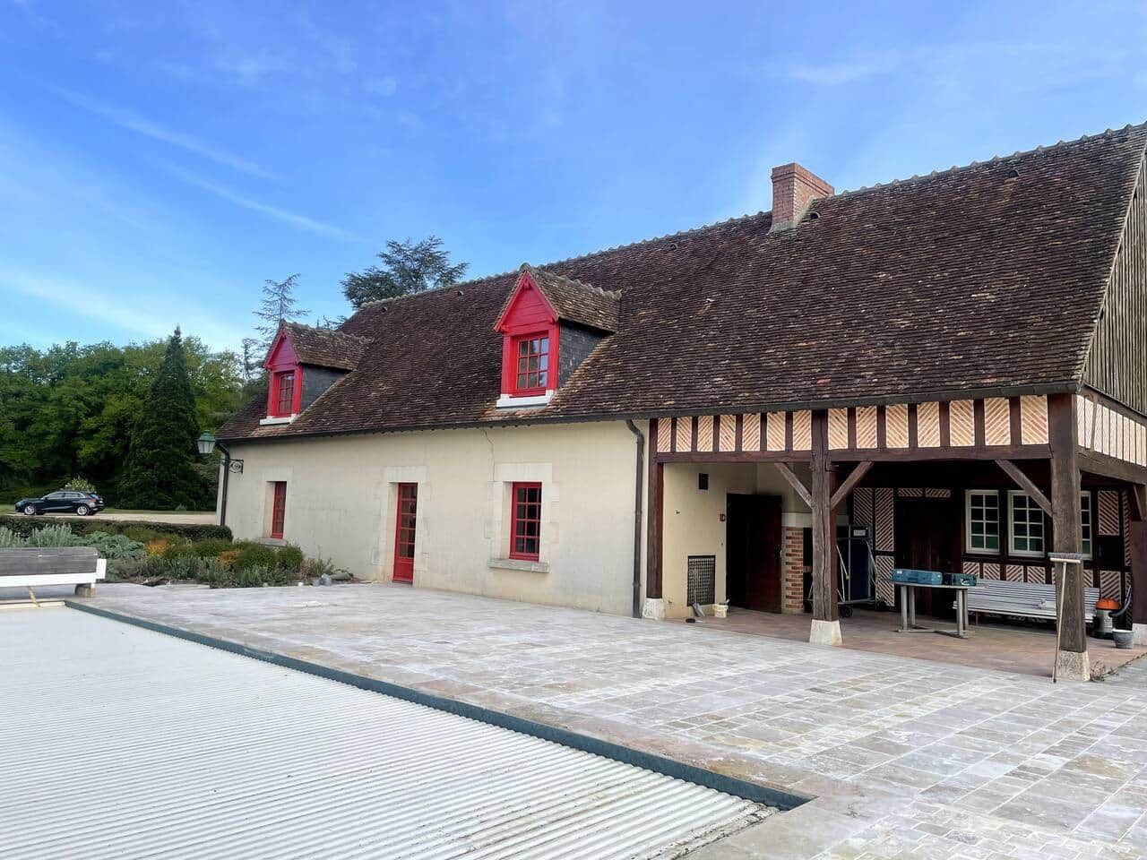 Een traditioneel gebouw met een pannendak, een overdekte veranda en een klein bijgebouw met een rode deur.