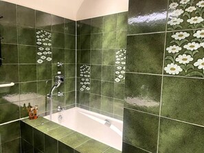 Une salle de bain avec des carreaux verts, une baignoire et une douche.
