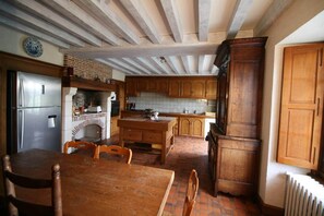 Une cuisine avec des meubles de rangement en bois, une cheminée en briques et une table à manger avec des chaises.