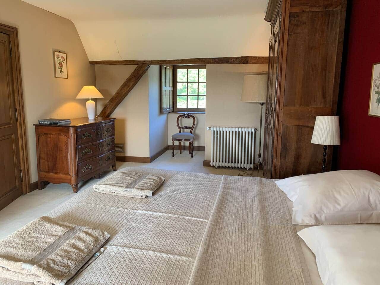 A bedroom with a large bed, a wooden dresser, a chair, and a radiator.