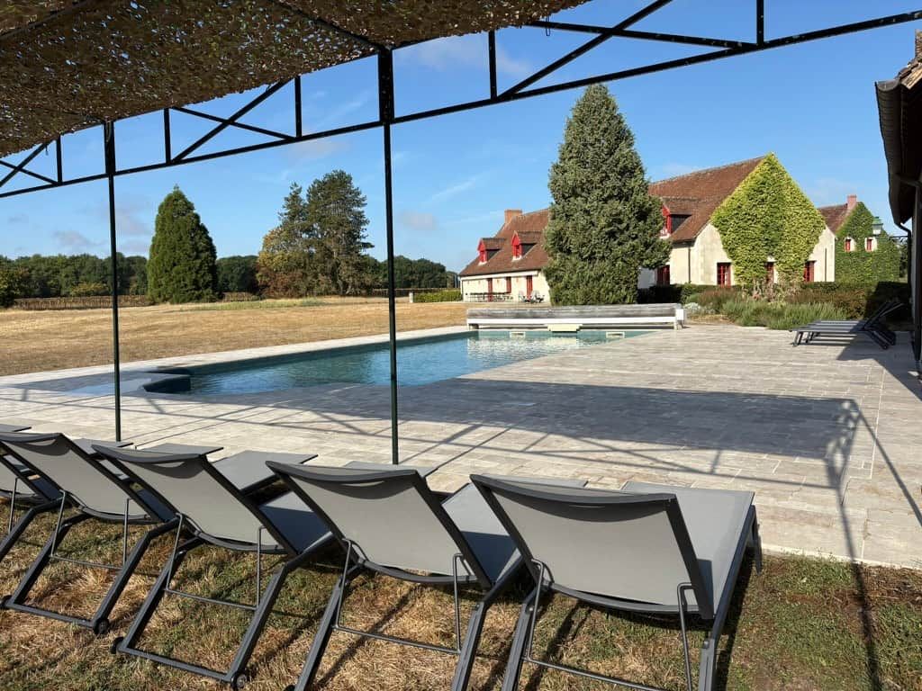 Un espace piscine avec des chaises longues et une vue sur un bâtiment dont les murs sont recouverts de lierre.