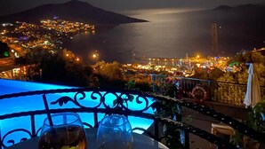 Vista nocturna desde un balcón con una mesa, dos vasos y una barandilla.