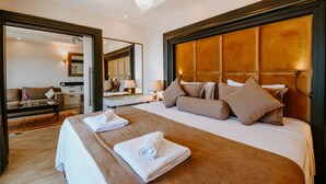 Habitación de hotel con una cama grande, una sala de estar con sofá y mesa de centro, y un espejo que refleja la habitación.