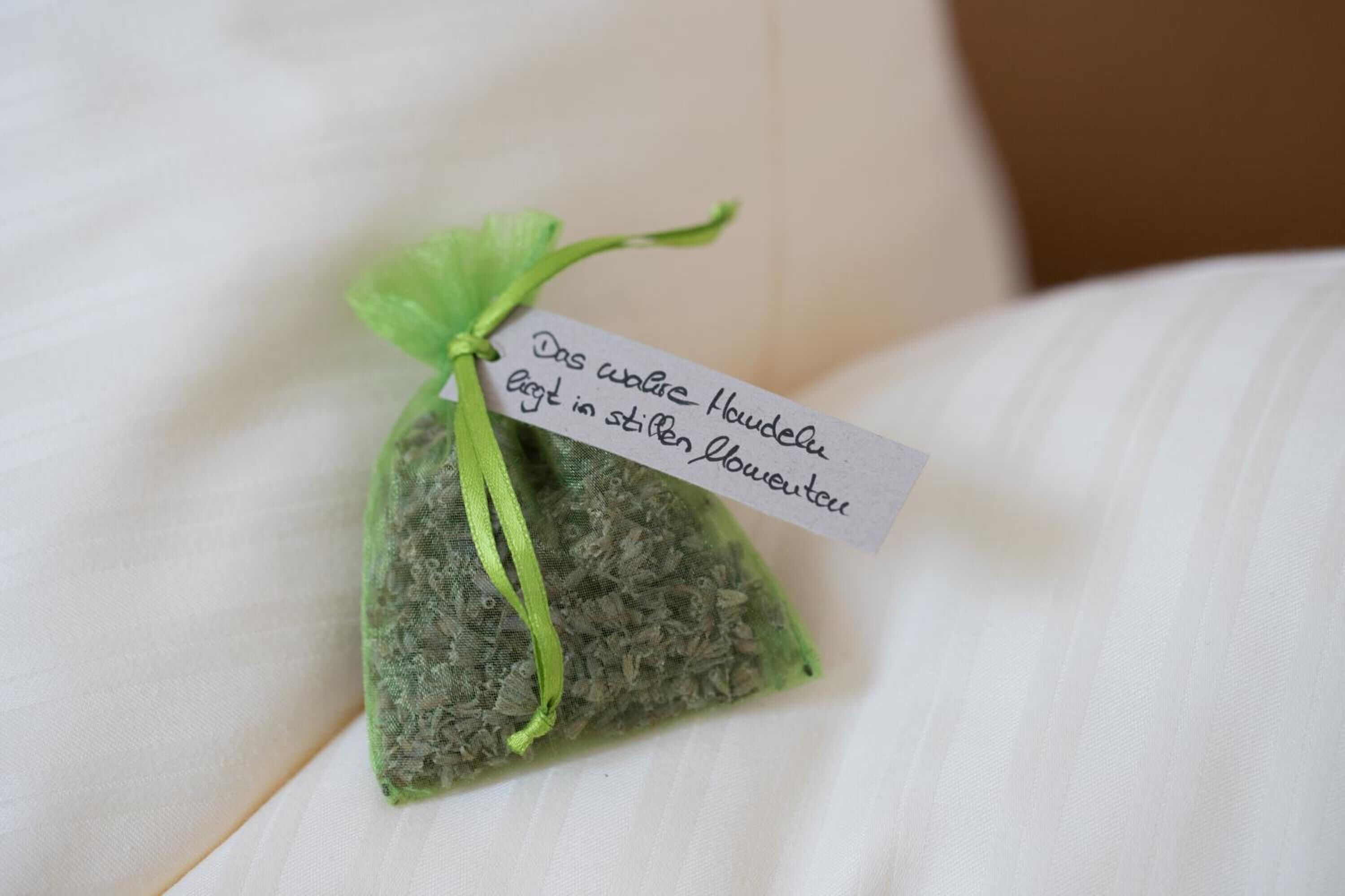A small green sachet tied with a green ribbon, containing a handwritten note in German.
