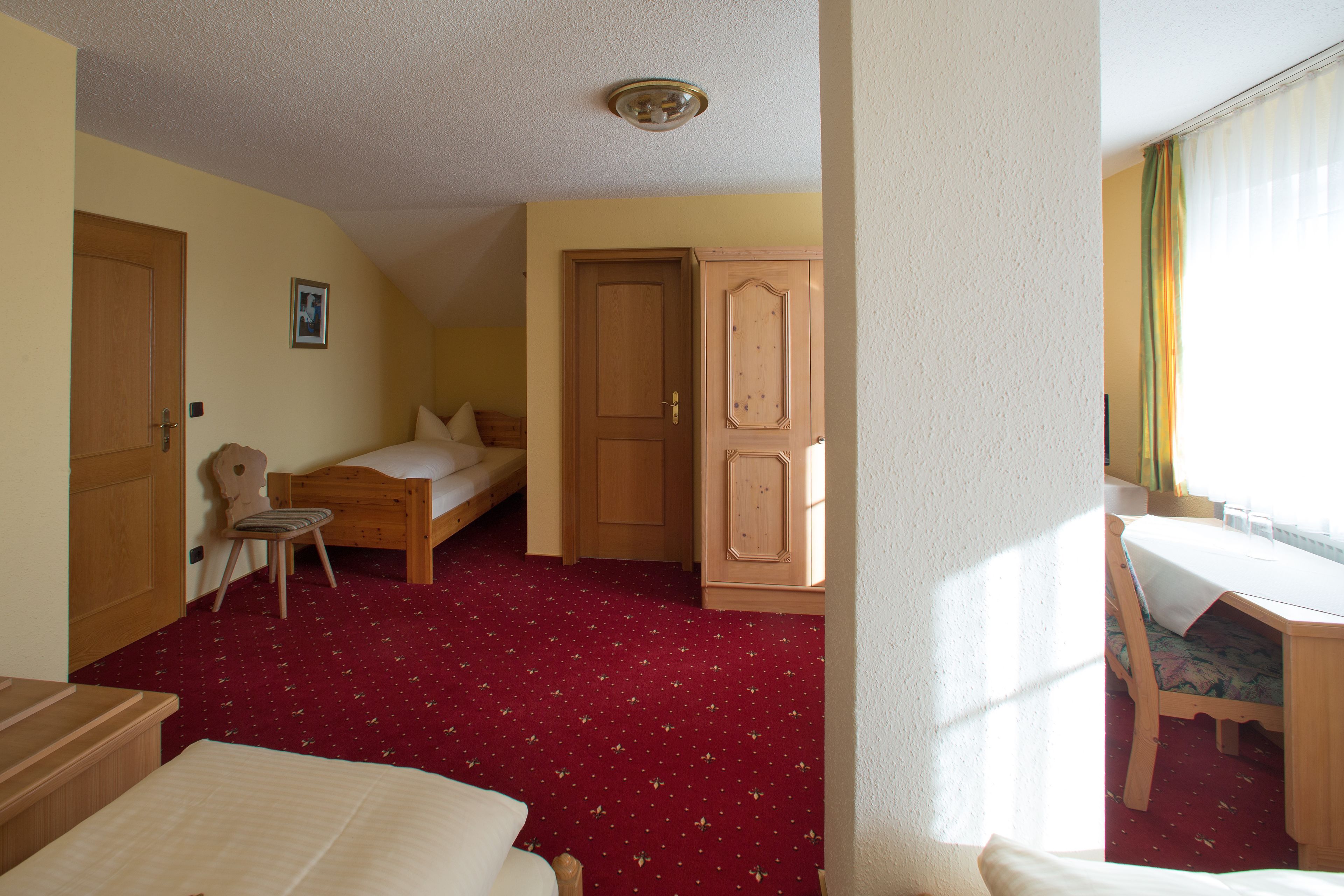 Ein Hotelzimmer mit rotem Teppich, Holzmöbeln, einem Bett, einem Schreibtisch und einem Kleiderschrank.