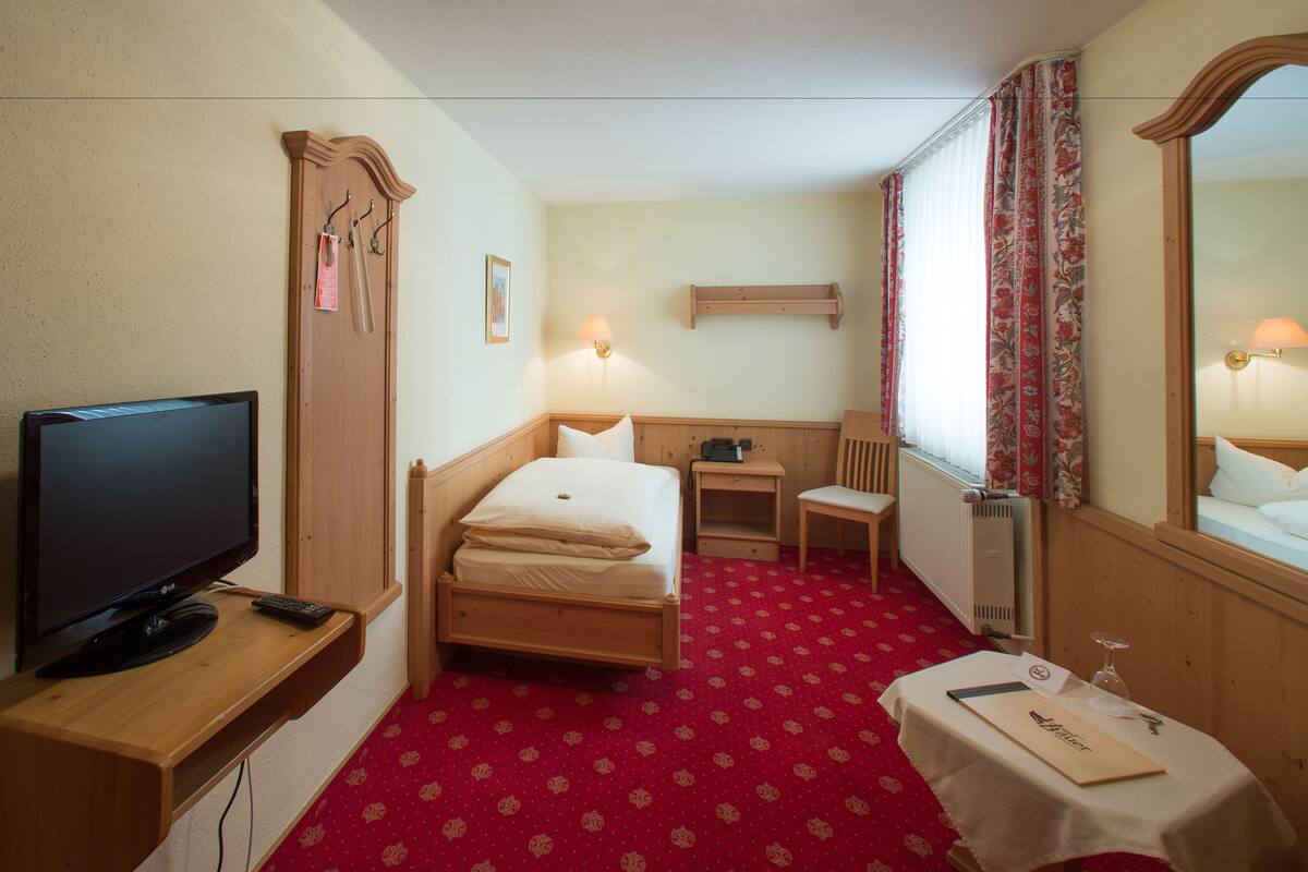 A hotel room with a bed, a desk, a chair, a television, and a mirror.