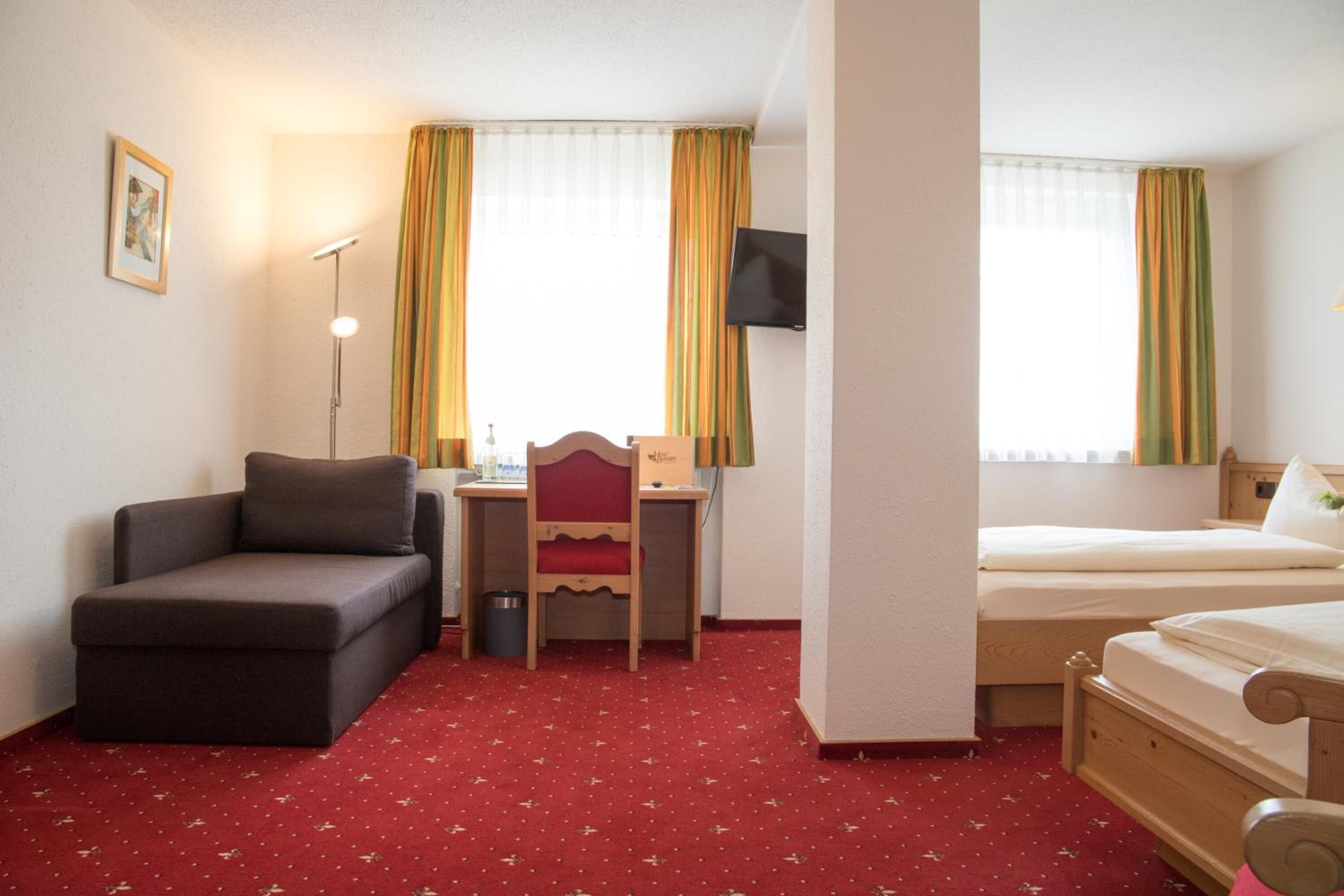 Une chambre d’hôtel avec un lit, un bureau et une chaise, un canapé et un téléviseur fixé au mur.