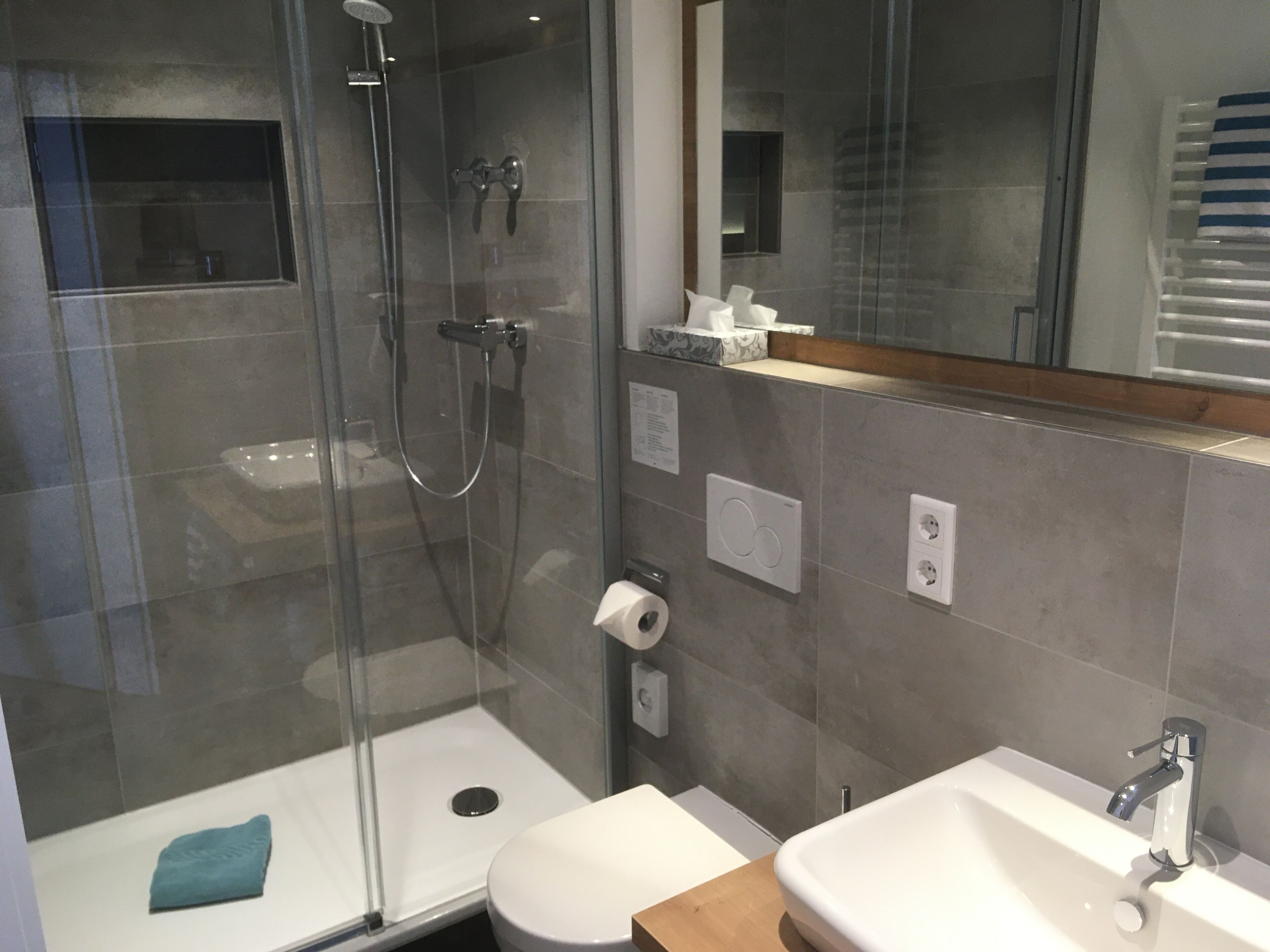 Ein modernes Badezimmer mit einer Duschkabine, einer Toilette und einem Waschbecken mit Spiegel darüber.