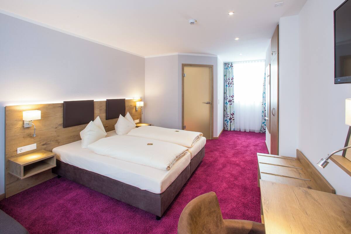A hotel room with a large bed, two bedside tables, a desk, and a chair.