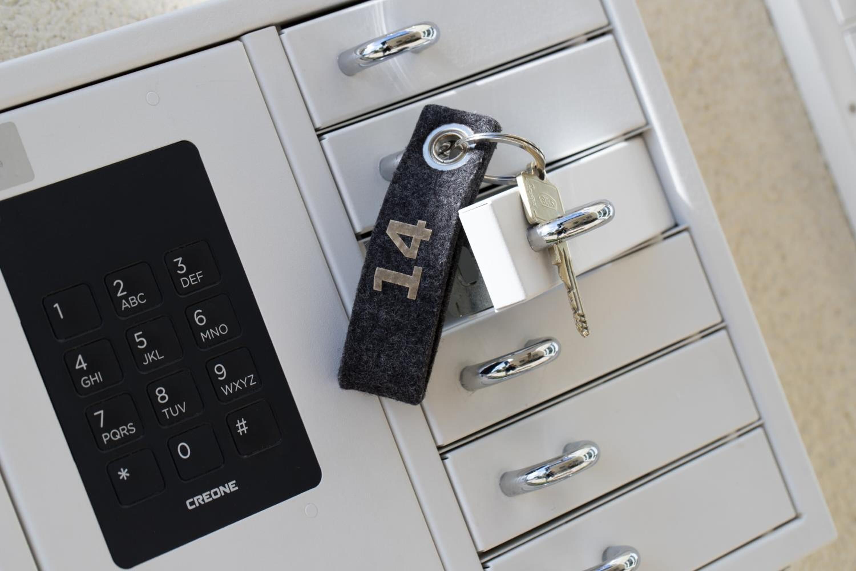 A keypad lock with a number pad and a keychain with a padlock on a white cabinet with drawers.