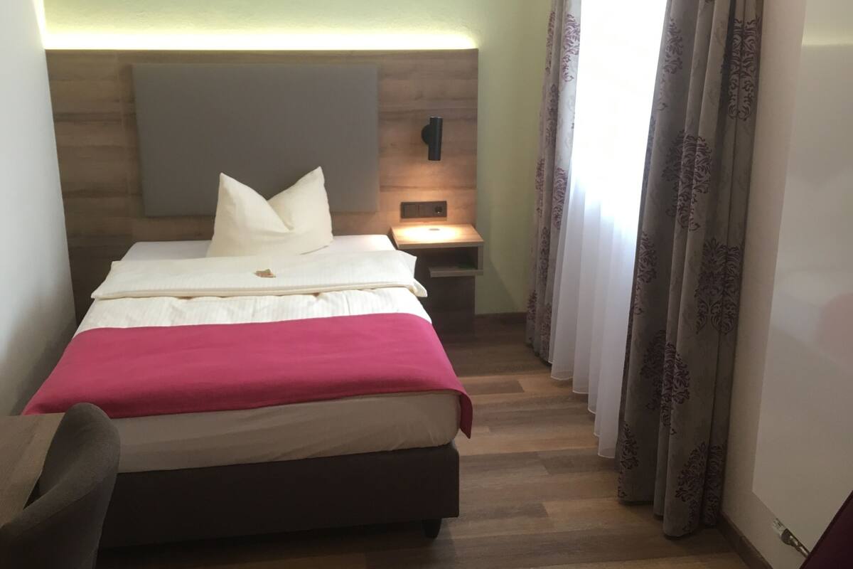 A hotel room with a bed, bedside table, and a chair.