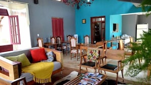 A cozy living room with a sofa, wooden chairs, a coffee table with magazines, and a dining area with a table and chairs. - Pousada Santa Maria (Tiradentes)