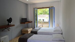 A room with two beds, a TV, a small fridge, and a window with a view of a house. - Pousada Santa Maria (Tiradentes)