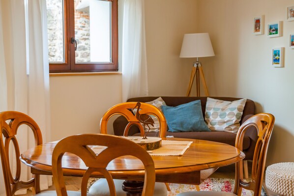 A cozy living room with a wooden dining table, chairs, a sofa with cushions, a floor lamp, and a window with curtains. - cottage "The stork" on the wine route - Kientzheim (Kaysersberg vineyard) (Kaysersberg Vignoble)
