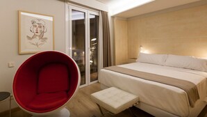 A modern hotel room with a large bed, a red chair, a small table, and a sliding glass door leading to a balcony. - San Gil Plaza Hotel (Zamora)