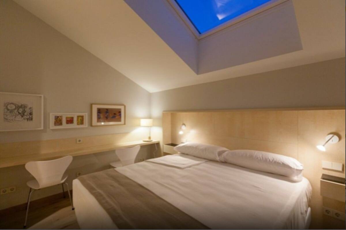 Una habitación de hotel con tragaluz, una cama, un escritorio y una silla.