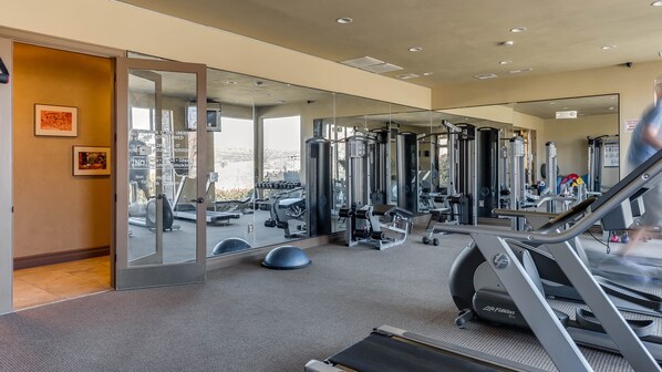 Un gimnasio con máquinas de cardio, estaciones de pesas y espejos en las paredes.