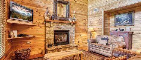 A cozy cabin interior with a stone fireplace, wooden walls, a leather sofa, and a television mounted on the wall.
