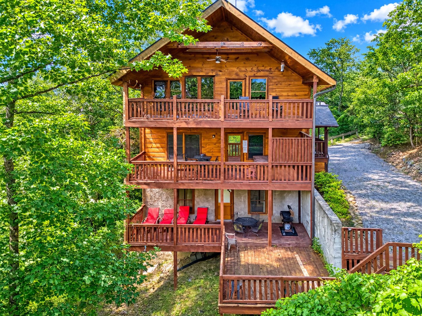 A multi-story wooden cabin with balconies, outdoor seating, and a gravel path.