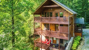 Une cabane en bois à plusieurs étages, dotée de balcons et entourée d’une forêt dense.