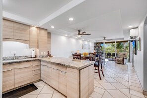 A modern kitchen with a central island, wooden cabinets, and a dining area with a view of palm trees.
