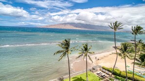 A beach with clear blue water, palm trees, and a mountain in the background. - Menehune Shores #401 4th floor Ocean View, A/C throughout, Great Rates (Kihei)