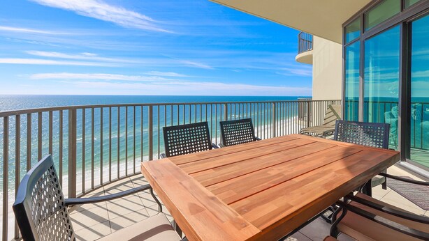 A balcony with a wooden table and chairs, overlooking the ocean.