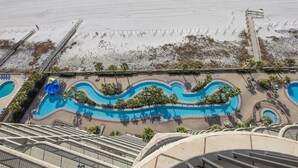 An aerial view of a resort with a large swimming pool, palm trees, and a beach area.