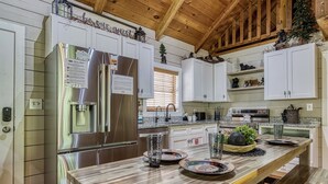 A modern kitchen with stainless steel appliances, white cabinetry, and a wooden dining table. - A frame of Mind- 10 minutes to Dollywood!  Hot tub, Wifi, Free tickets! (Sevierville)