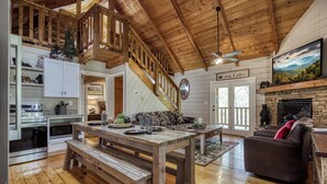 A cabin interior with a wooden staircase, a dining area with benches, a fireplace, and a cozy seating area. - A frame of Mind- 10 minutes to Dollywood!  Hot tub, Wifi, Free tickets! (Sevierville)