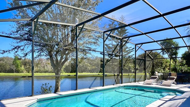 Une piscine offrant une vue dégagée sur un lac et des arbres, entourée d’un espace abrité avec des chaises.