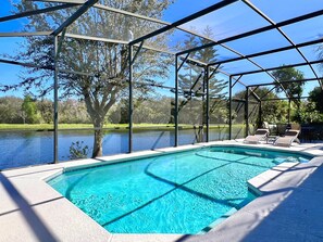 Piscina com vista clara para um lago e árvores, cercada por uma área coberta com cadeiras.