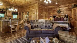 A cozy log cabin interior with a wooden dining area, a sofa with animal-themed cushions, and a bed with a rustic headboard. - Pooh Bear, Hot Tub, WIFI, $560 FREE tickets each paid day!!! (Sevierville)