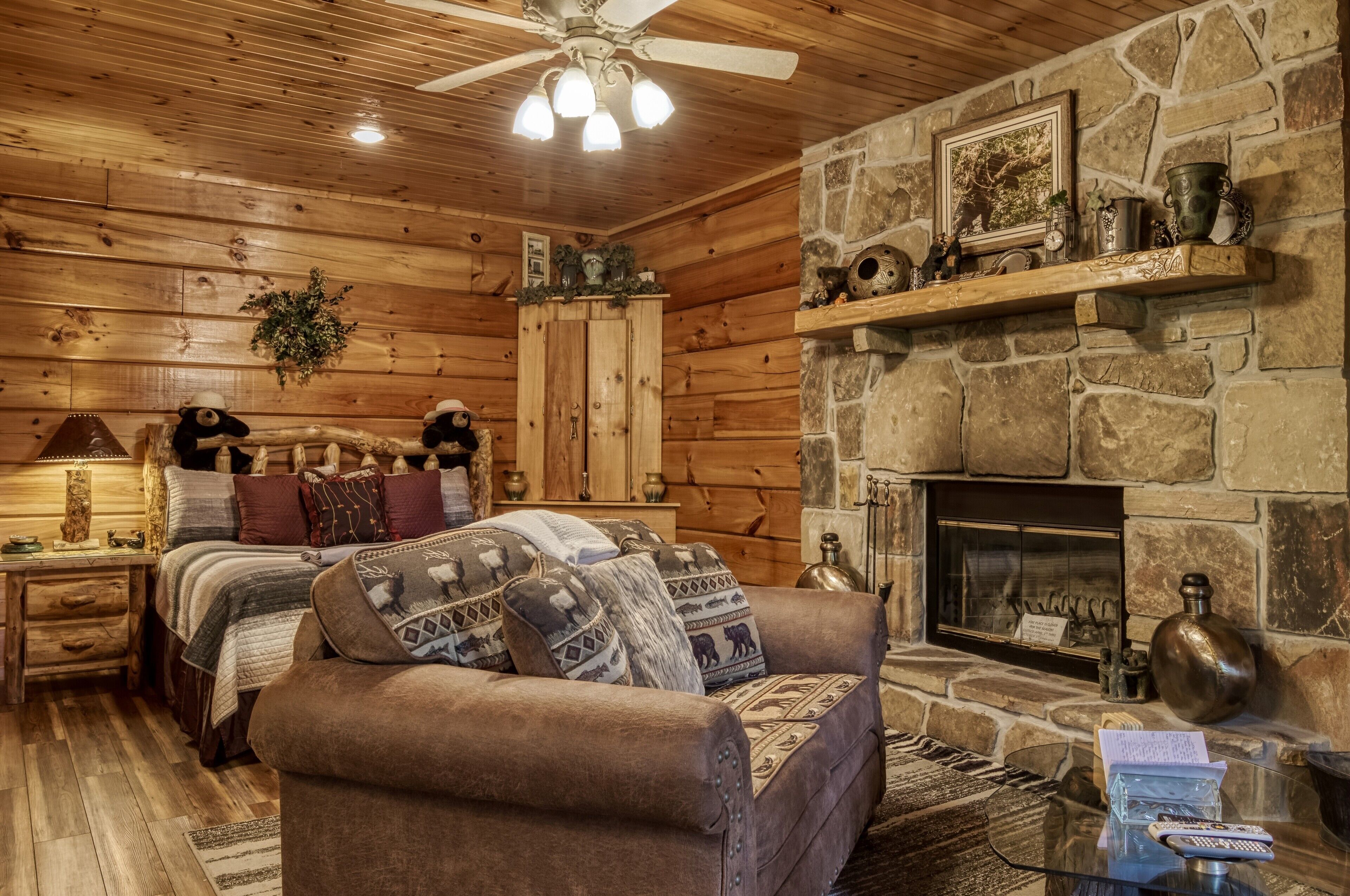 Une pièce chaleureuse aménagée dans un chalet en rondins, avec un lit, un canapé, une cheminée et un ventilateur de plafond.