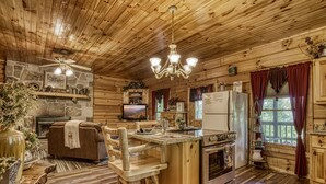 A rustic cabin interior with a stone fireplace, wooden furniture, a kitchen with a refrigerator, and a dining area with a wooden table and chairs. - Pooh Bear, Hot Tub, WIFI, $560 FREE tickets each paid day!!! (Sevierville)
