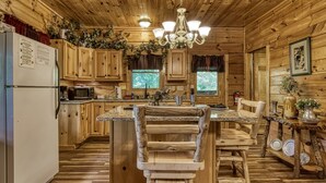 A rustic kitchen with wooden cabinets, a central island with a wooden chair, a chandelier, and a refrigerator. - Pooh Bear, Hot Tub, WIFI, $560 FREE tickets each paid day!!! (Sevierville)