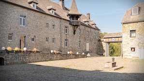 Ein historisches Steinhaus mit einem zentralen Turm, einem Innenhof mit Kopfsteinpflaster und einem kleinen Brunnen.
