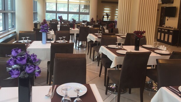 Un restaurante con varias mesas dispuestas, cada una con platos, vasos y cubiertos. Amplias ventanas permiten el ingreso de luz natural, y el techo cuenta con iluminación empotrada.