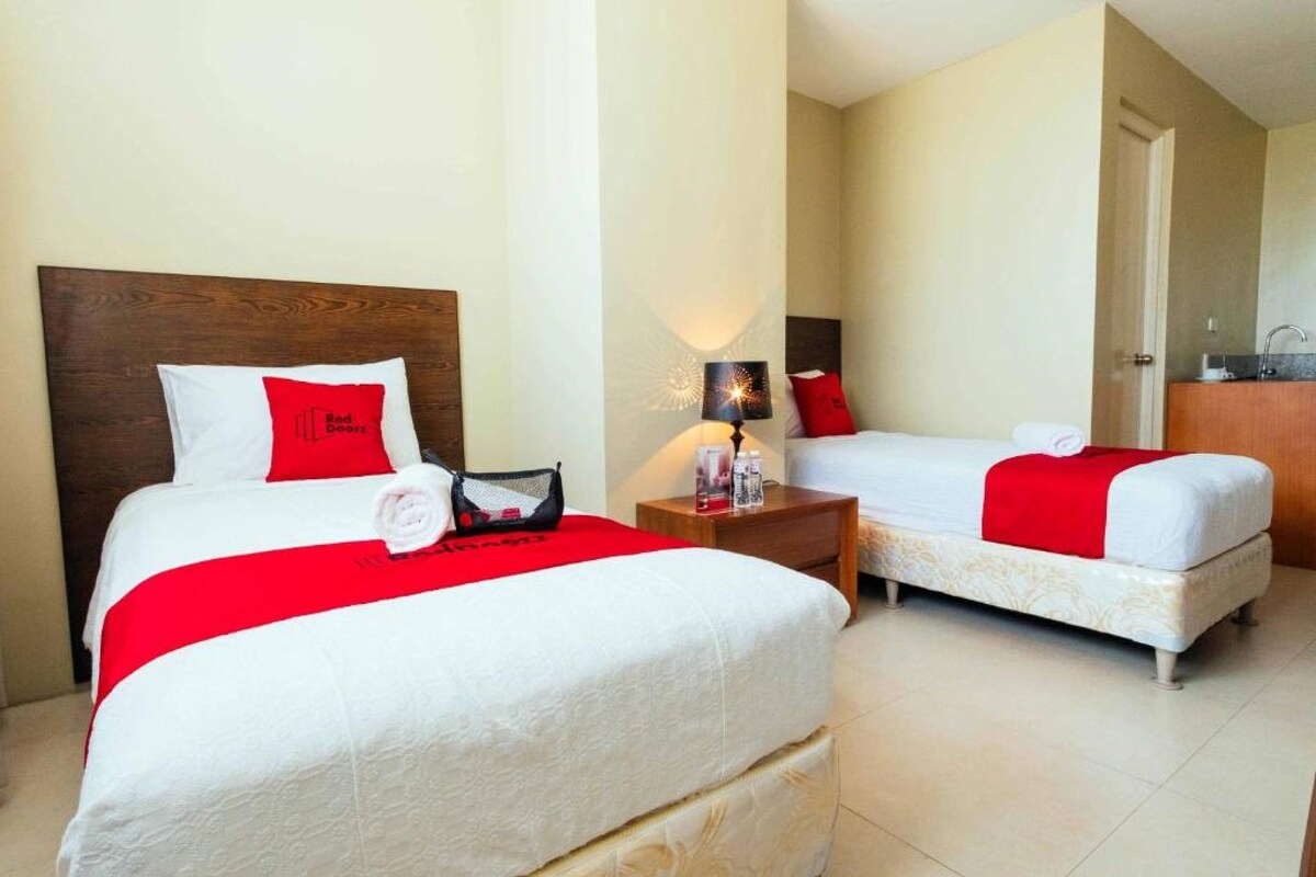 A hotel room with two beds, each with a red and white bedspread, a wooden headboard, and a nightstand with a lamp.