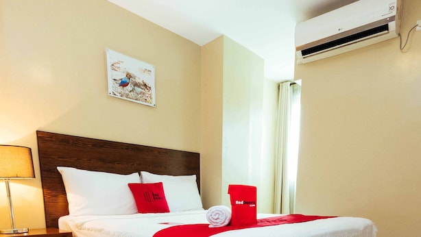 Habitación de hotel con una cama grande, una mesita de noche, una lámpara, aire acondicionado instalado en la pared y una ventana con cortinas.