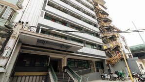 Un edificio de varios pisos con una planta baja comercial, una escalera que conduce a los pisos superiores y un letrero que indica locales comerciales a la derecha.