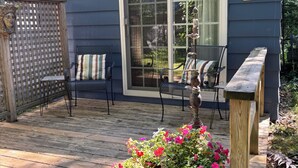 En overdækket terrasse med en træbænk, en potteplante med blomster og en dekorativ genstand på et stativ.