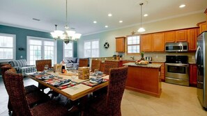 A spacious kitchen with wooden cabinets, a central island, and a dining area with chairs and a table set for a meal. - Summer Wind- An island getaway in the perfect location. (Holmes Beach)