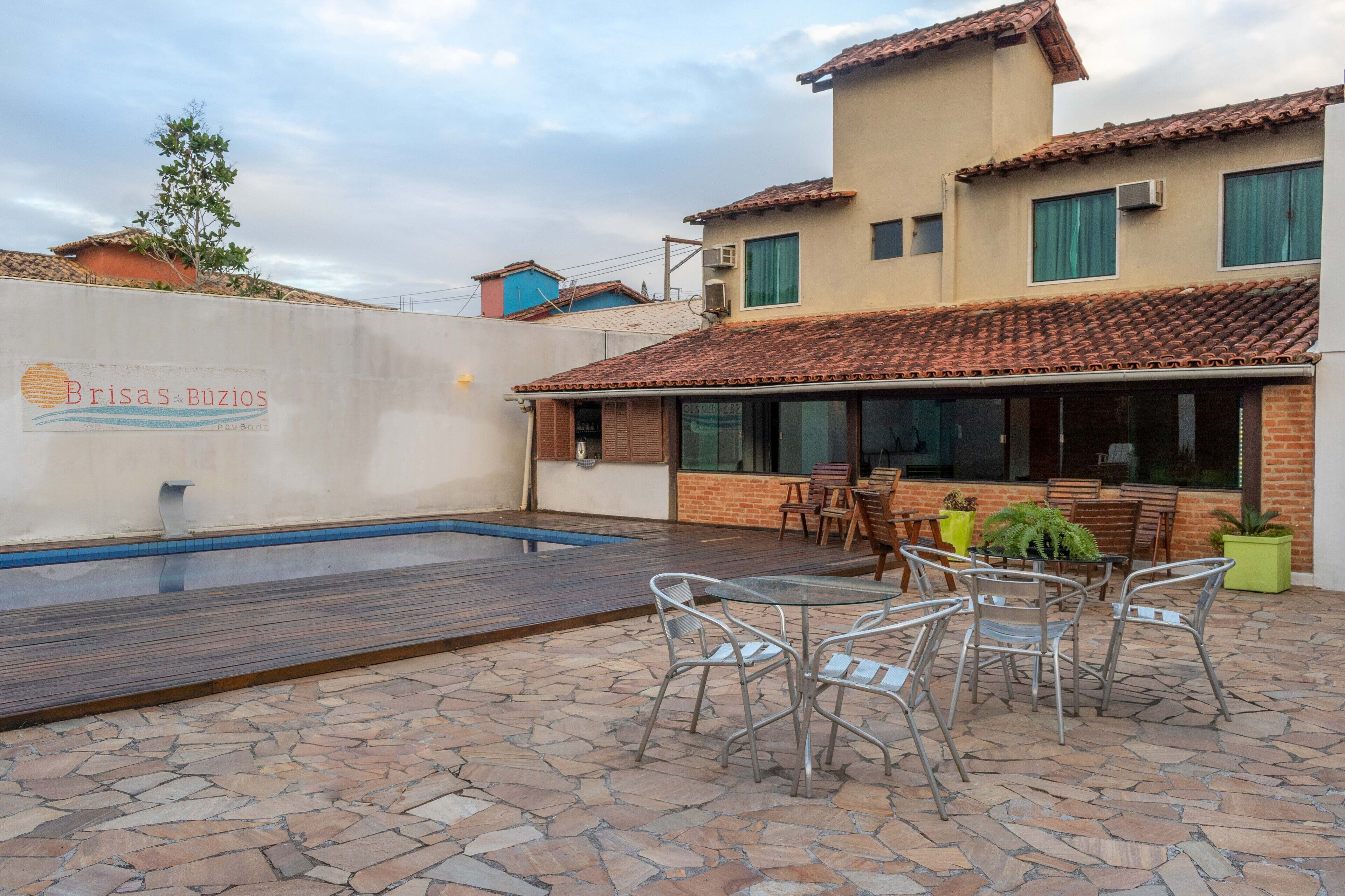 Un área de piscina con una mesa y sillas en la terraza, una piscina y un edificio con tejado de azulejos y ventanas.