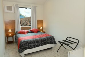 A bedroom with a bed, two bedside lamps, a window with curtains, a radiator, and a chair. - Pousada Brisas de Buzios (Búzios)